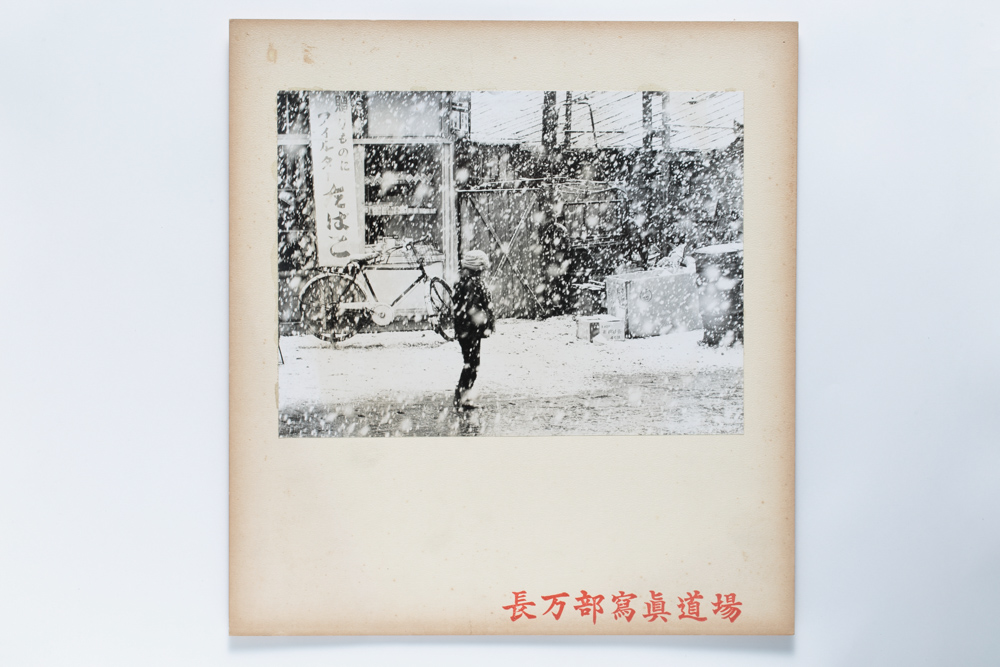 画像：<p>撮影年不詳(1962(昭和37)年以前)<br />
本町、長万部町<br />
舗装される前の駅前商店街通り。澤博の自宅である長万部食堂を背にして撮影されている。<br />
澤は雪が降っている情景を好んで撮影しており、本作は澤が撮影した可能性が高い。</p>
